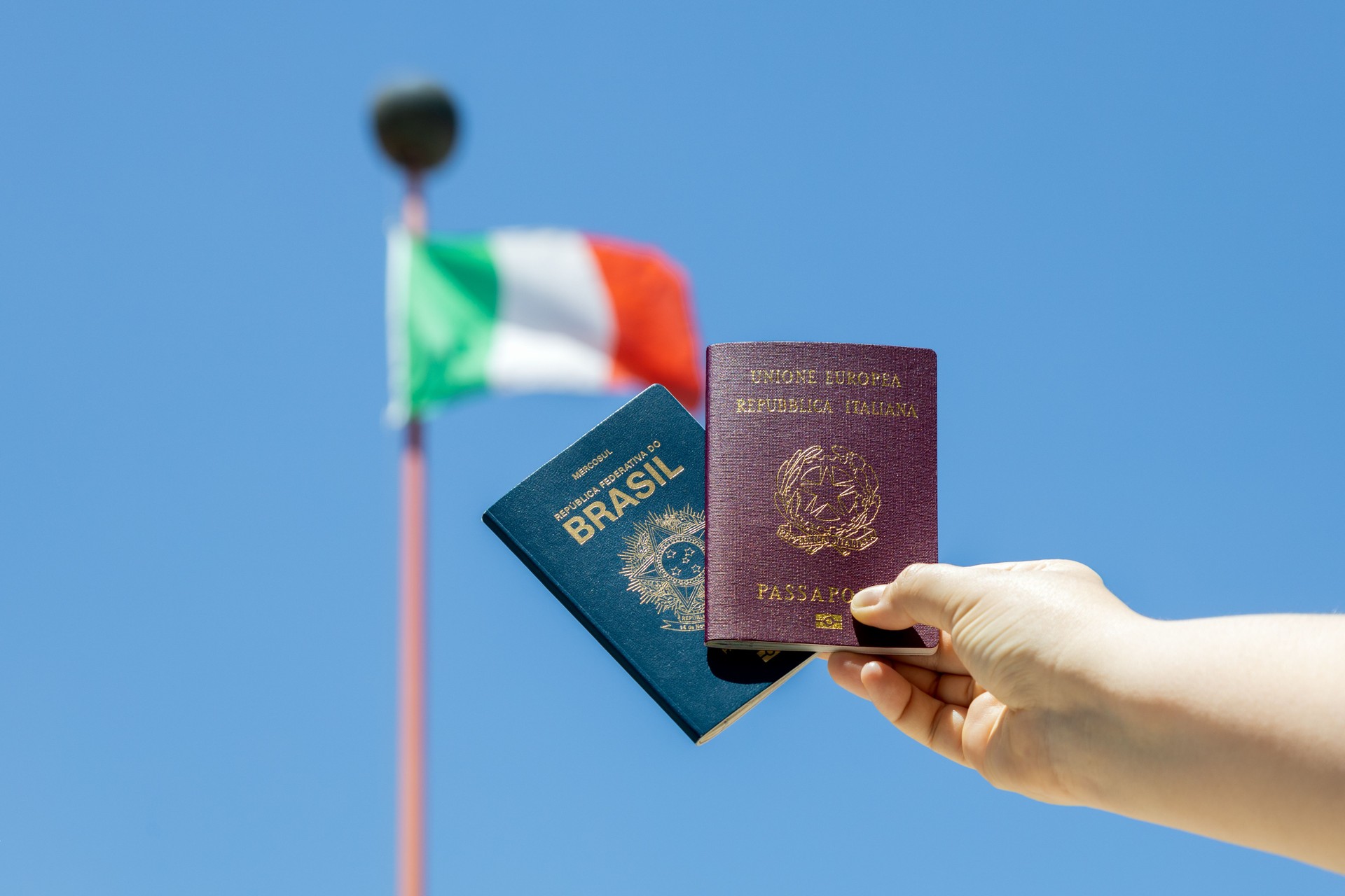 Hand holding Brazilian and Italian passport with Italian flag in the background